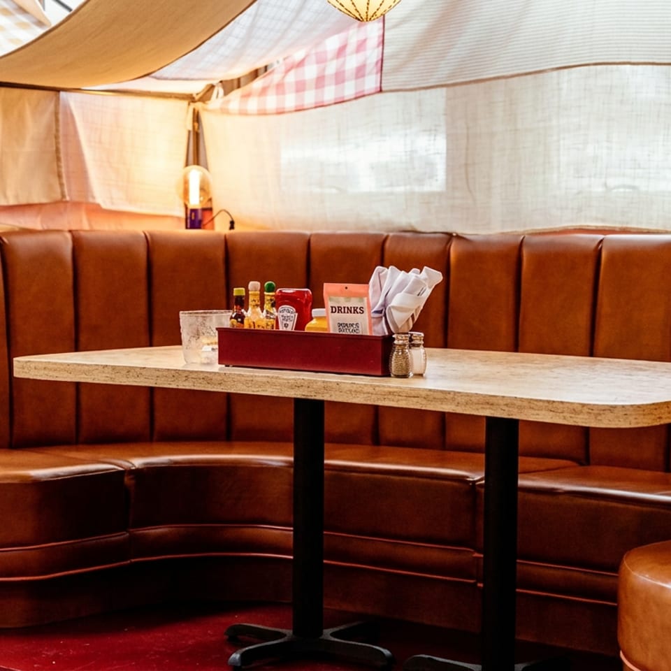 Warm restaurant booth with leather seating, a wooden table, condiments, napkins, and patterned fabric canopy overhead.